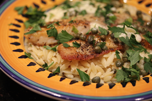 Yellow and blue rimmed pasta bowl with orzo, pan cooked tilapia, capers and parsley