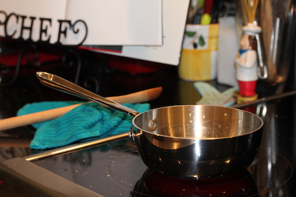 Small saucepan sitting on a glass cooktop with a cookbook on a stand in the background