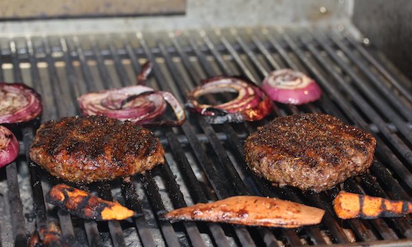 Grill grates topped with burgers, sweet potatoes and thick red onion slices