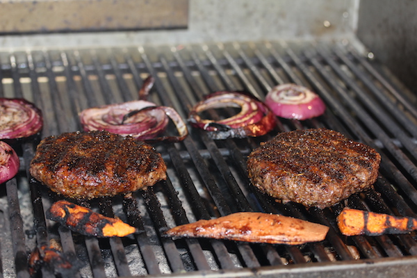 Grill grates topped with burgers, sweet potatoes and thick red onion slices