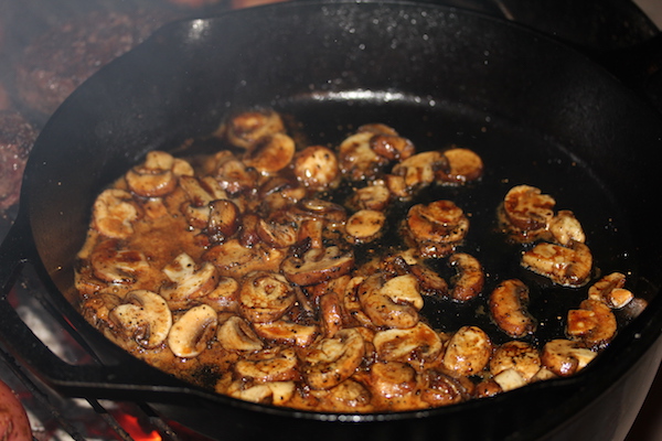 A cast iron pan filled with mushrooms cooking on a charcoal grill