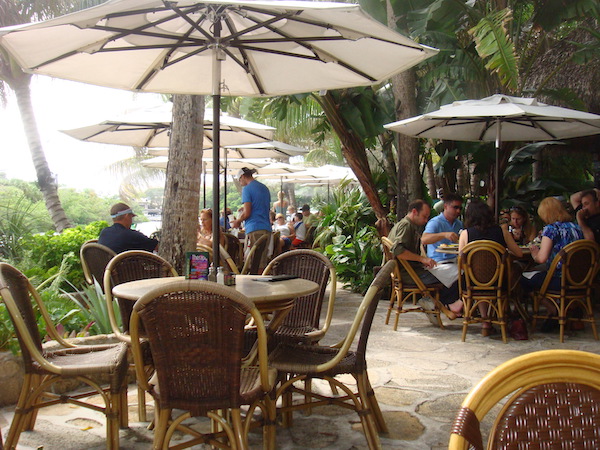 Palm trees, rattan dining tables and chairs and white market umbrellas
