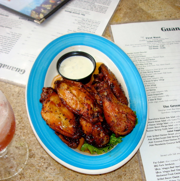 Menus and a blue rimmed platter with dark glazed chicken wings and a white dipping sauce