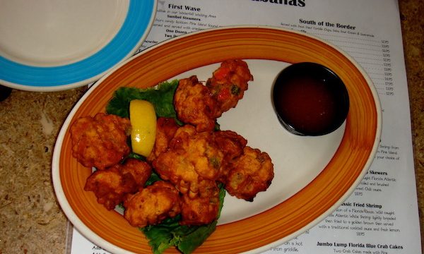 An oval pumpkin colored rimmed platter with conch fritters and sauce