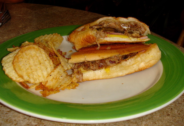 A lime green rimmed plate with a Cuban sandwich and chips