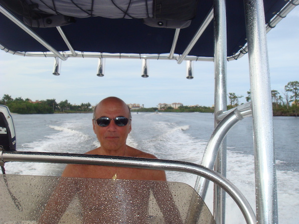 A bald headed man with sunglasses steering a speed boat