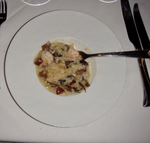 large white plate with deep well in center filled with risotto, shrimp, andouille sausage and mushrooms