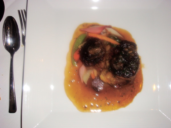 White plate filled with two veal medallions, golden brown sauce and root vegetables