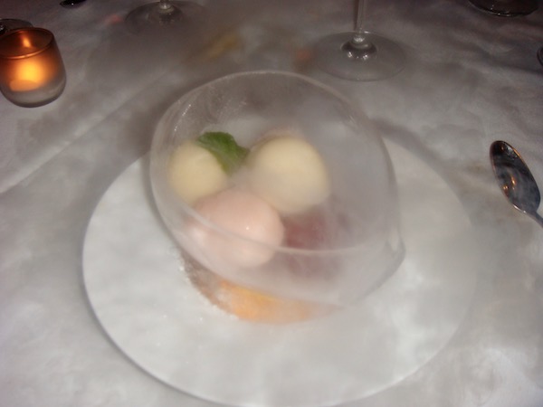 White plate holding a crystal bowl made of ice that's filled with several small balls of various fruit sorbets