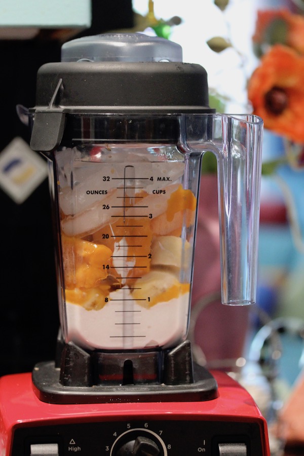 The jar of a blender filled with mango chunks, banana slices, ice and milk