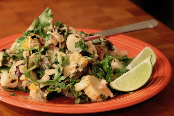A persimmon dinner plate piled high with salad greens, hearts of palm slices and crabmeat with a creamy dressed and two lime wedges on right side of plate