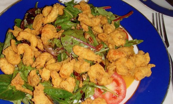 A cobalt blue dinner plate topped with fried shrimp and salad greens.
