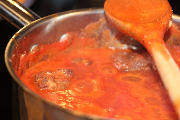 Red sauce simmering in a pan with meatballs and a wooden spoon resting on top of pan