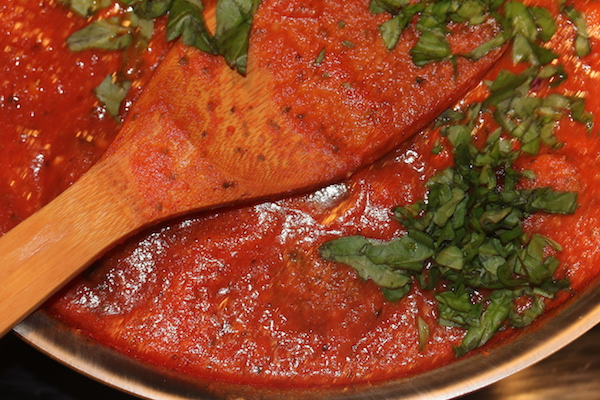A pan filled with red sauce, meatballs and fresh basil with a wooden spoon