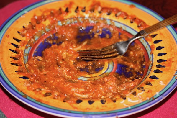 A yellow and blue pasta dish with the remains of red sauce and a fork