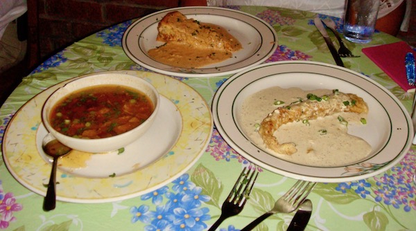 Floral print tablecloth set with a bowl of gumbo, a plate of alligator tenderloin and a wedge of savory cheesecake