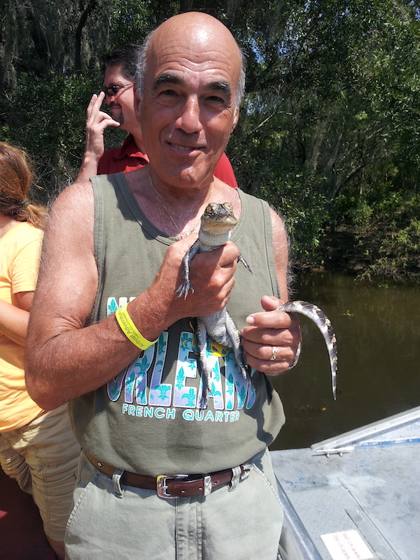 A man in an olive tank top holding a baby alligator.