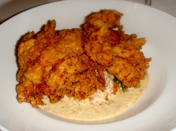 A white dinner plate topped with golden brown fried chicken sitting atop coleslaw and gravy