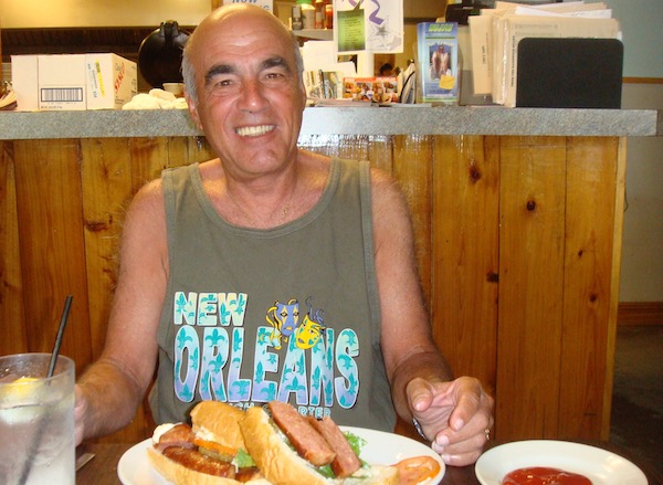 A man in an olive tank top smiling at his plate of food