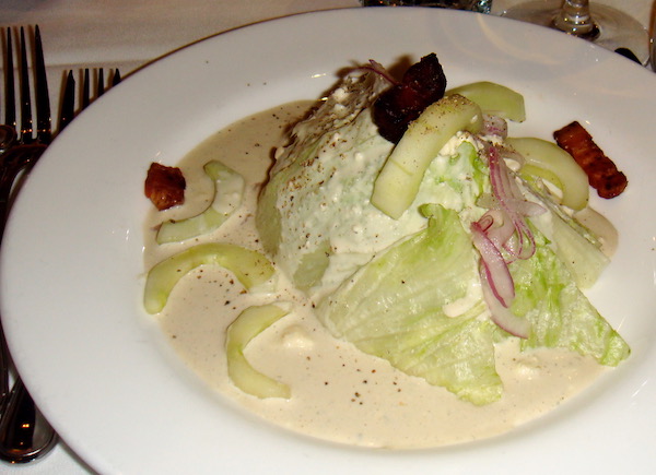A white plate with a wedge of iceberg lettuce, dressing and slivers of red onion