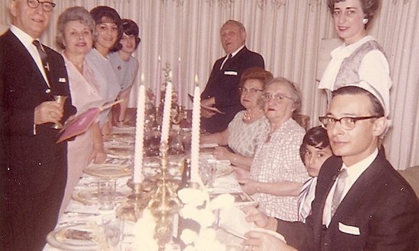 A family standing and seated around a dining room table set for a Passover seder.