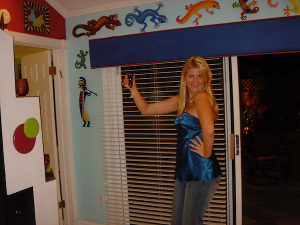 A blond woman holding a glass to toast standing in front of sliding glass doors with assorted art lizards above it
