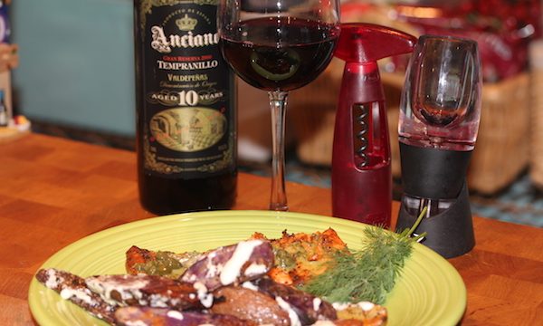 Yellow plate with fingerling potatoes and steelhead trout both drizzled with white sauce. Plate is on a butcher block and behind plate is a bottle of wine, a wine glass half filled with red wine and a red corkscrew.