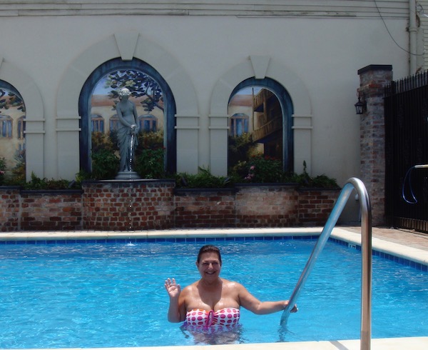 A dark haired woman in a pink and white bathing suit waving from a swimming pool