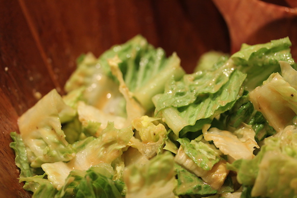 A wooden salad bowl filled with strips of Romaine lettuce that has a creamy golden colored dressing on it.