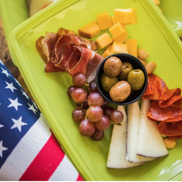 A lime green rectangular plate topped with cheese slices and cold cuts with grapes