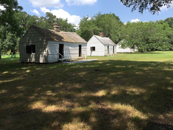Three little white shacks in a field with trees