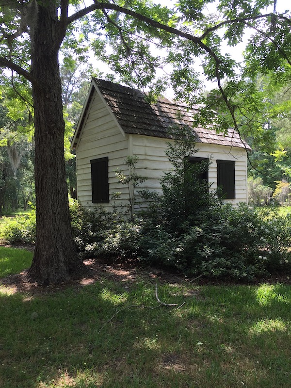 A little white shack in a field with trees