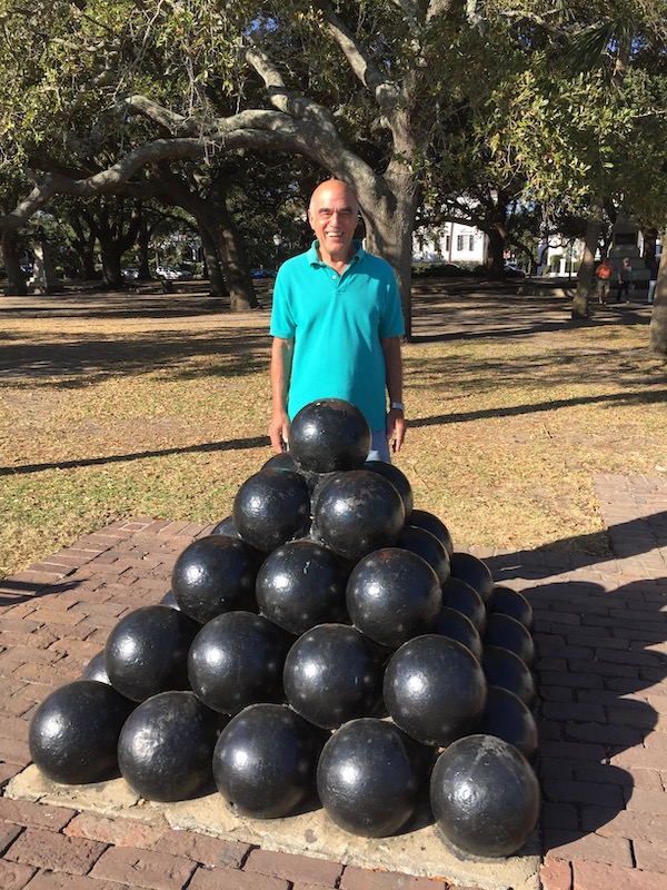 A man in a green shirt standing behind a pyramid of canon balls