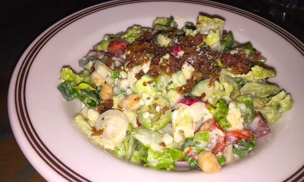 A white plate with a brown edge topped with a chopped salad and bacon