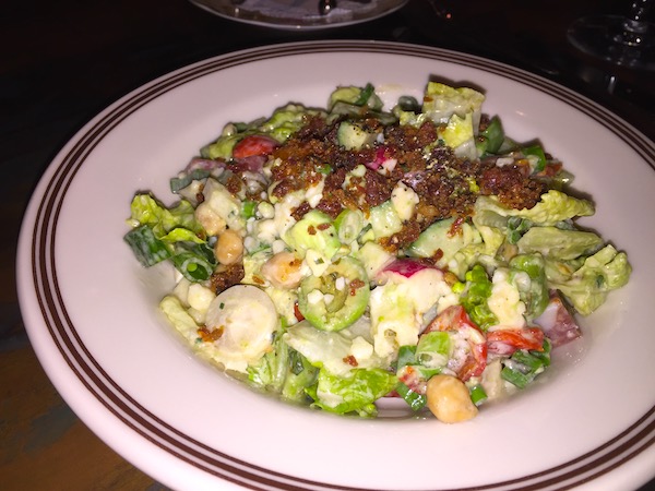 A white plate with a brown edge topped with a chopped salad and bacon