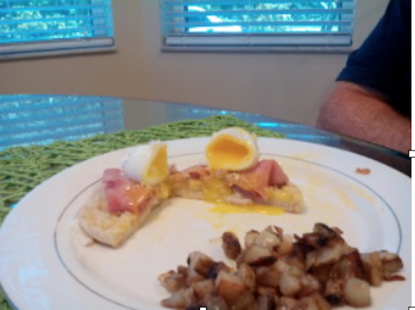 A large white plate with eggs benedict and home fries.