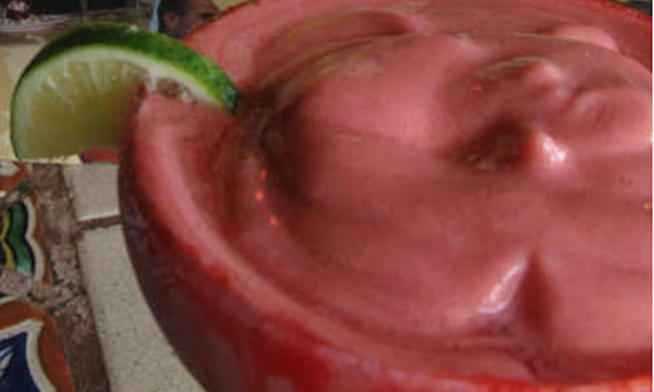 A margarita glass filled with frozen cranberry margarita with lime slice on rim of glass.