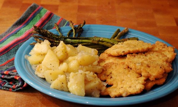 A turquoise plate topped with Salmon Croquettes and Potatoes with Roasted Asparagus sitting on a butcher block