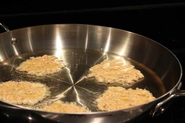 A frying pan with flattened spoonful of salmon batter frying