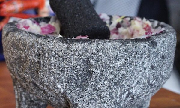 A lava rock mortar and pestle with chopped red onions in it sitting on a butcher block