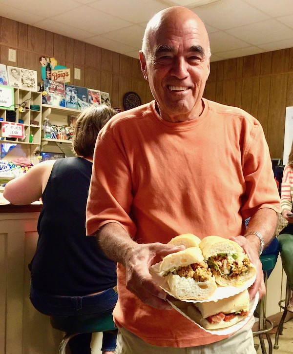 A man in an orange shirt carrying two plates of sandwiches