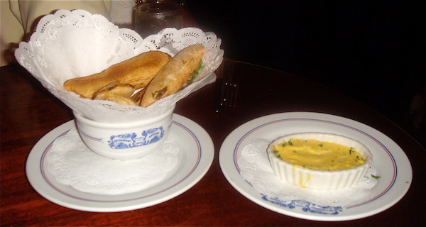 Wood table top with white and blue dishes holding soufflé potatoes and Bearnaise sauce