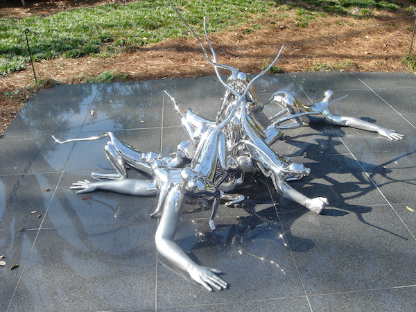 A surreal metal sculpture on pavement with lawn in the background
