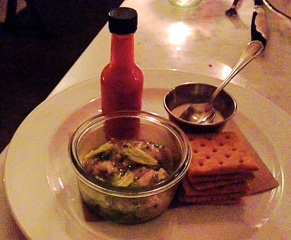 A table with a glass dish of Smoked Oysters with Saltines + Hot Sauce