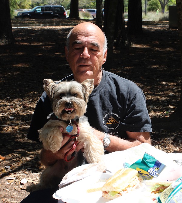 A man in a black t-shirt holding a black and gold Yorkie at a picnic table