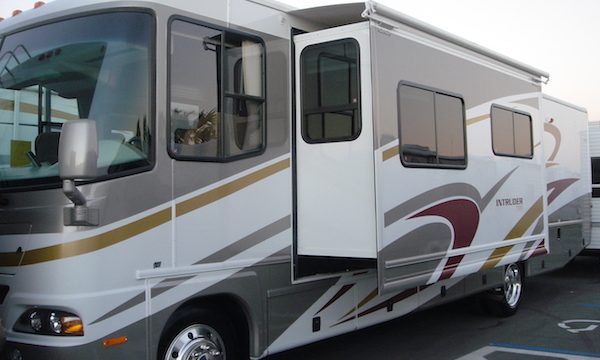 White, tan and gold Class A RV driver's side view with slide out
