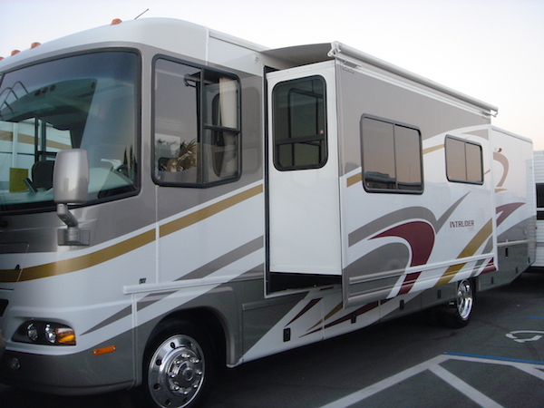 White, tan and gold Class A RV driver's side view with slide out