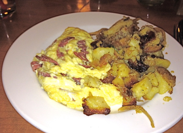 A white plate with cooked eggs and mushrooms and home fried potatoes on the side of the plate.