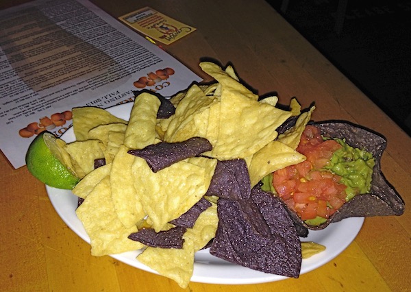 A white plate piled high with guacamole, blue and white corn tortilla chips and lime wedge.