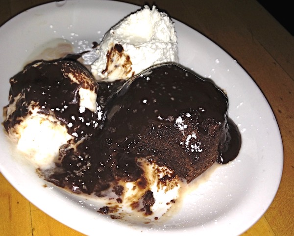 A white plate topped with a molten chocolate cake covered with fudge sauce and with whipped cream on the side.